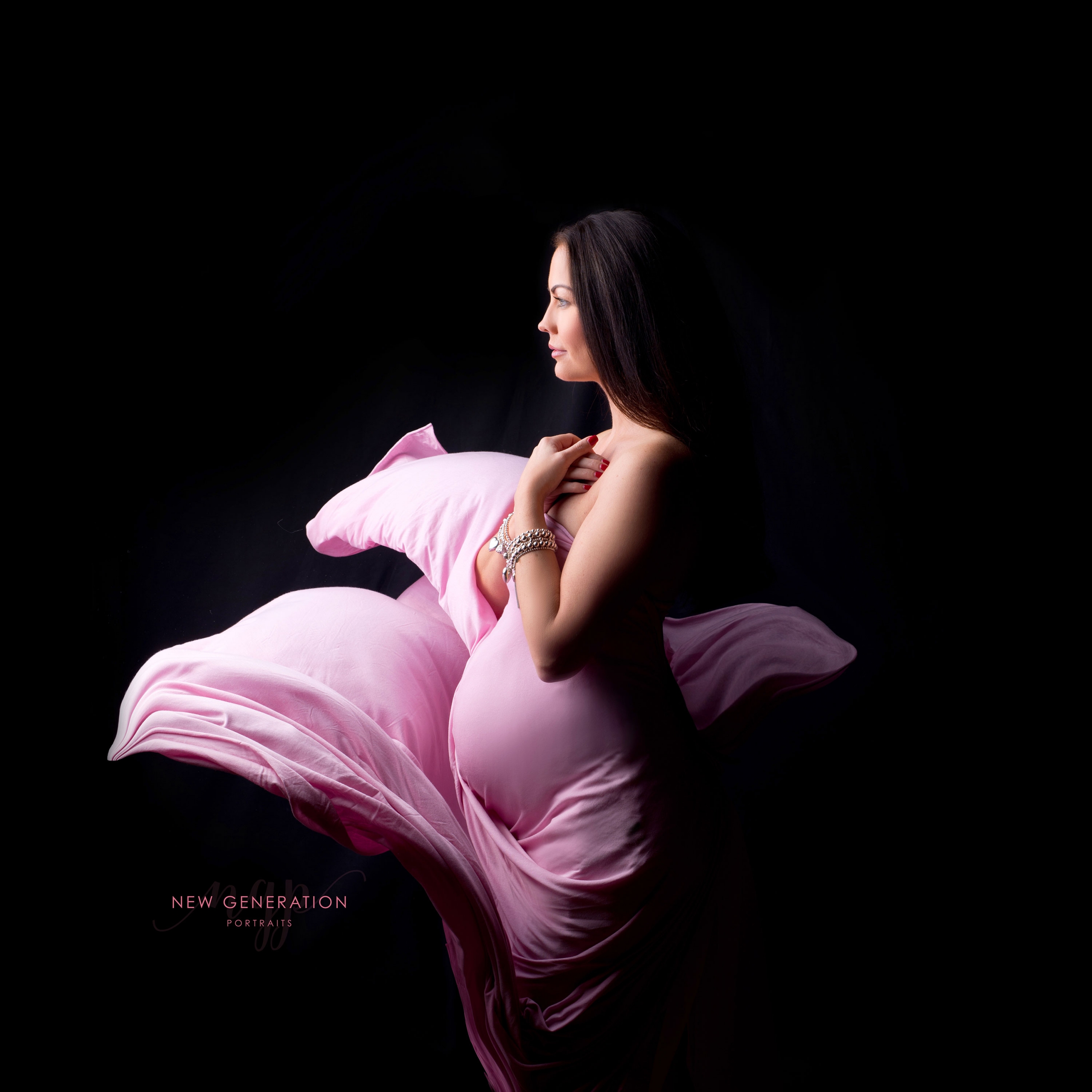 Pregnant lady side on covered in pink fabric on black background. Captured by New Generation Portraits