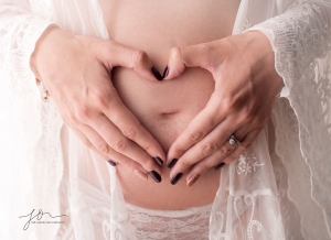 Hand making shapes of a heart in front of baby bump. Catoured by New Generation Portraits Cheshire