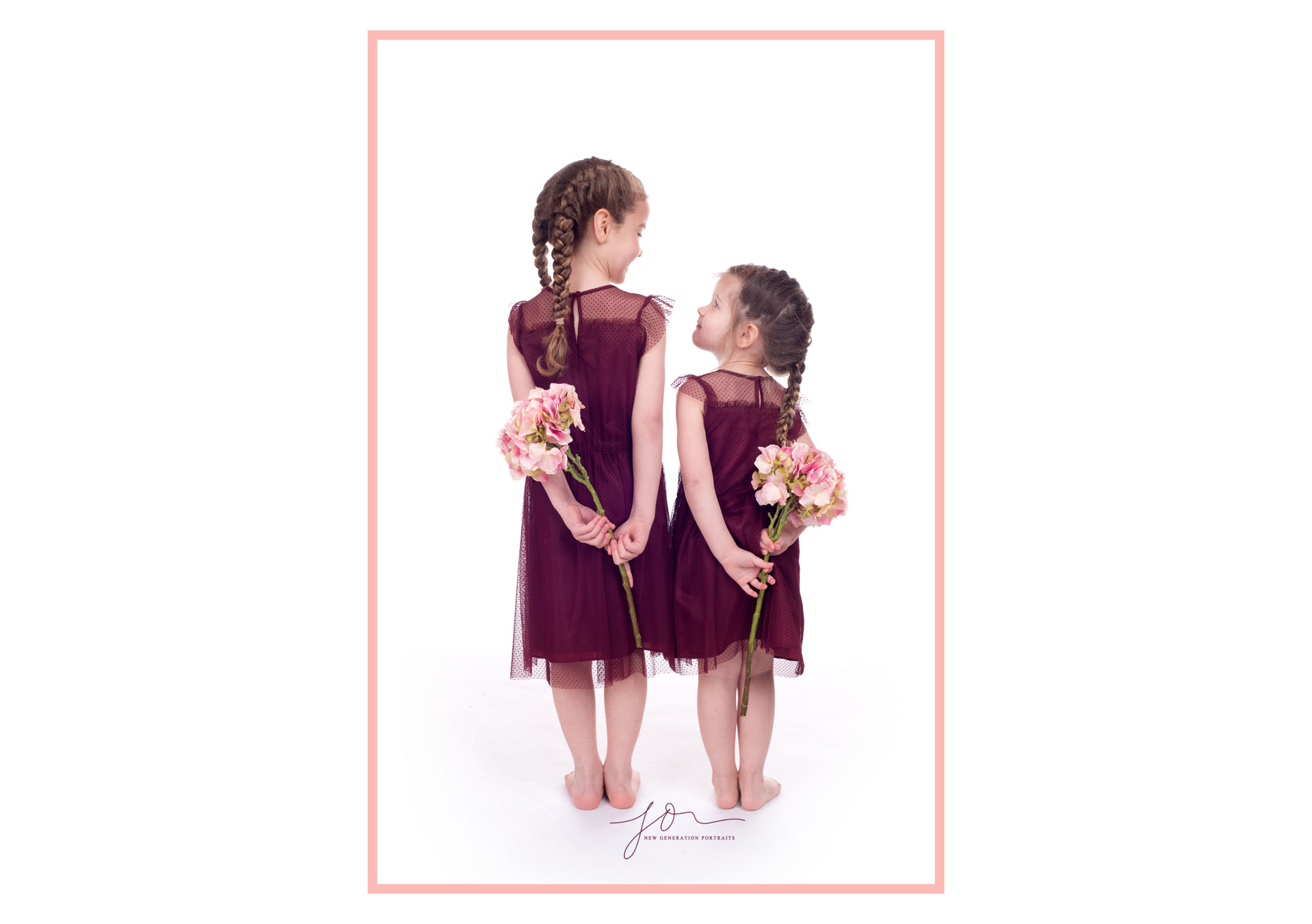 Sisters holding flowers behind their backs. Captured by New Generation Portraits