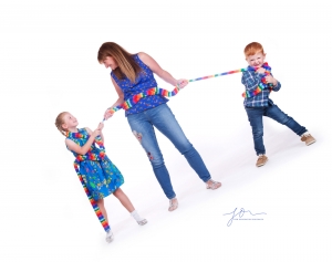 Laughing family mum and two children all tied together with colourful scarf. Captured by New Generation Portraits