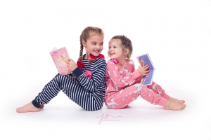 Sisters happily reading a book. Captured by New Generation Portraits