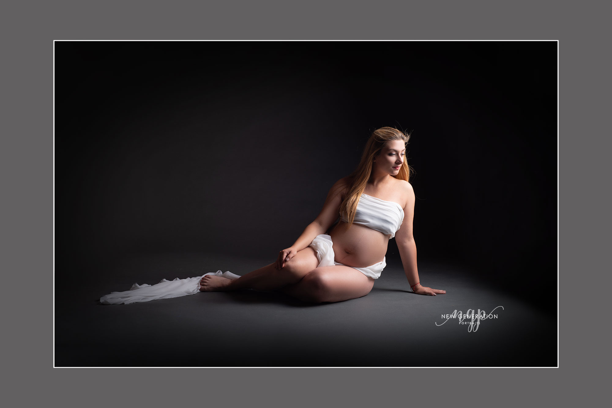 Pregnant lady sat on the floor with white fabric around her. Captured by New Generation Portraits.