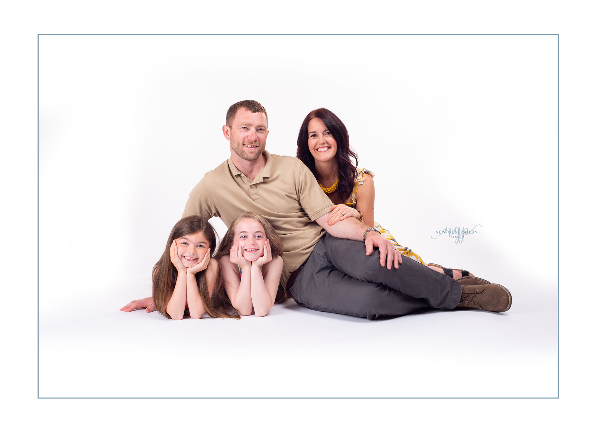 Happy family of four positioned on the floor of a white studio. Captured by New Generation Portraits.