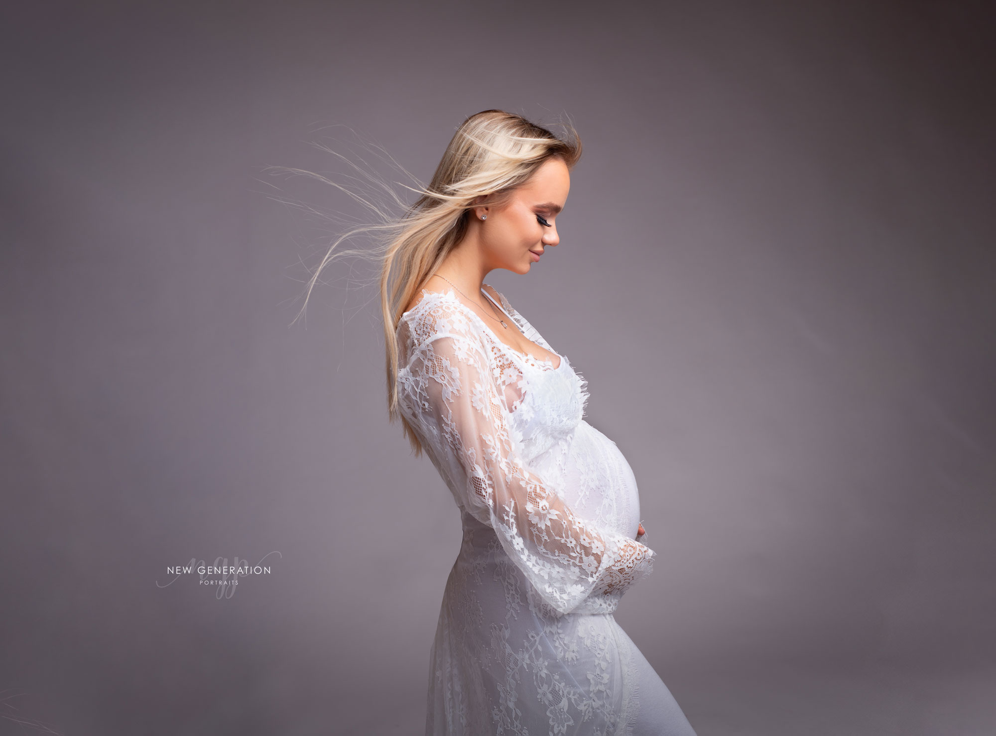 Timeless elegant maternity portrait in white dress with grey background captured at New Generation Portraits