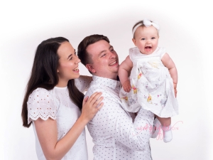 Family dressed in white with their your daughter laughing on a white background. Captured by New Generation Portraits